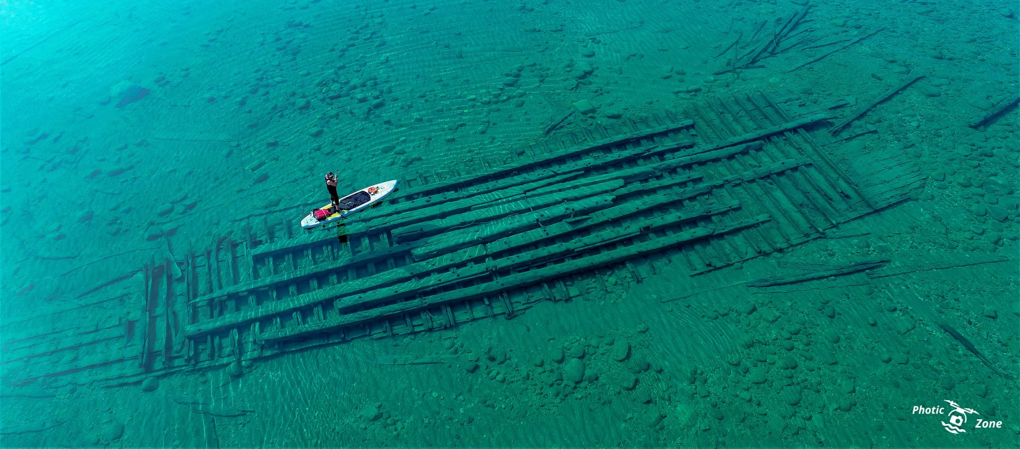 Paddleboarder gliding over a sunken shipwreck in the clear waters of Lake Michigan.