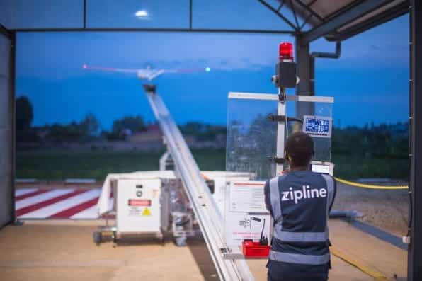 Zipline worker in a hi-vis vest stands at a drone launch catapult.