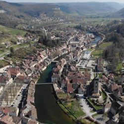 Aerial view of a French riverside town nestled in a green valley.