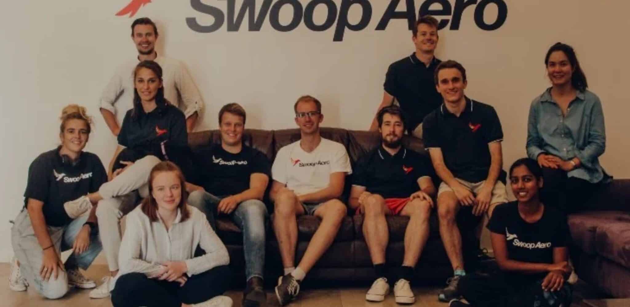 The Swoop Aero team posing together beneath the company logo in their office.