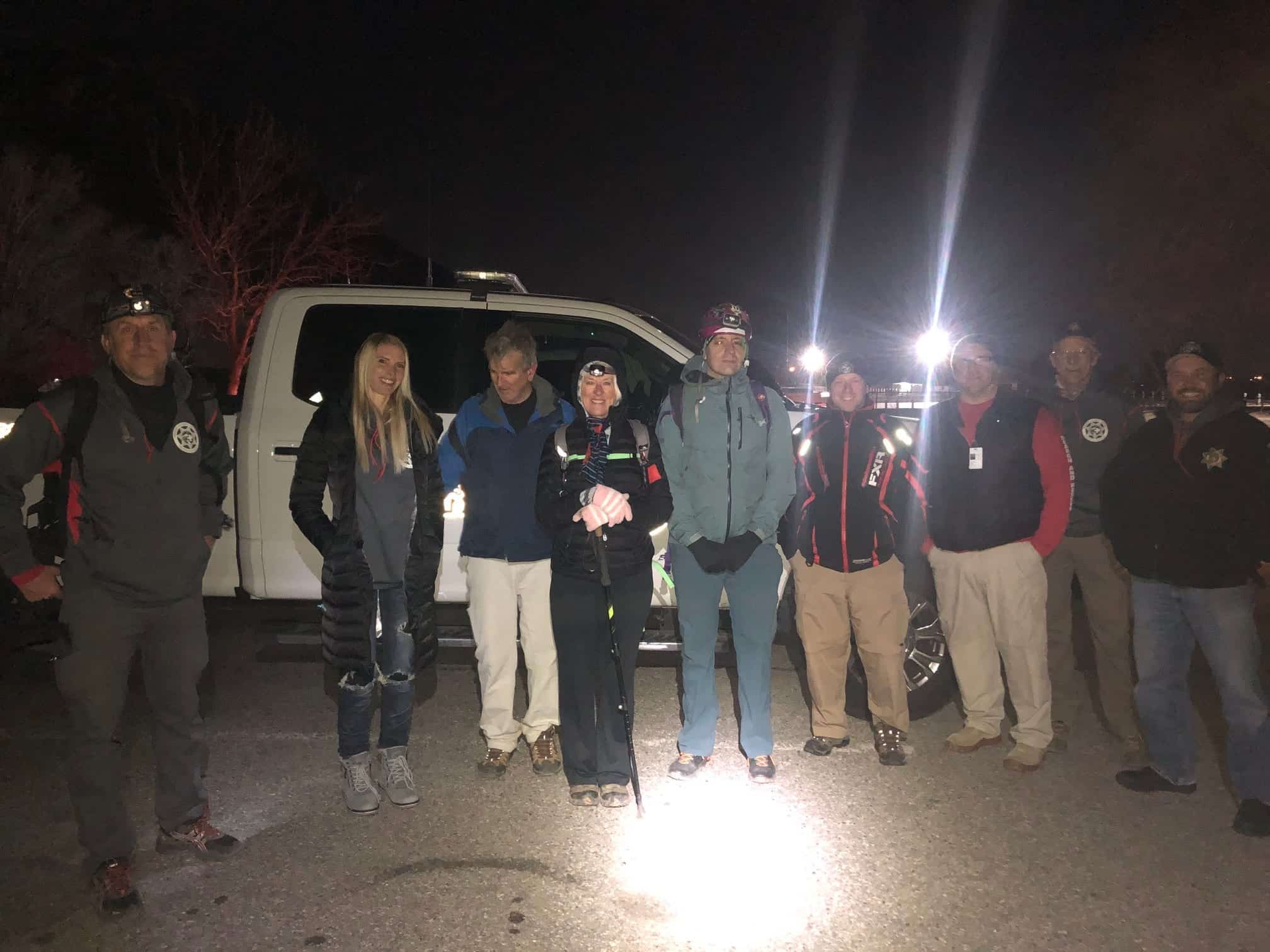 Search and rescue team stands with the recovered hikers beside a truck at night.