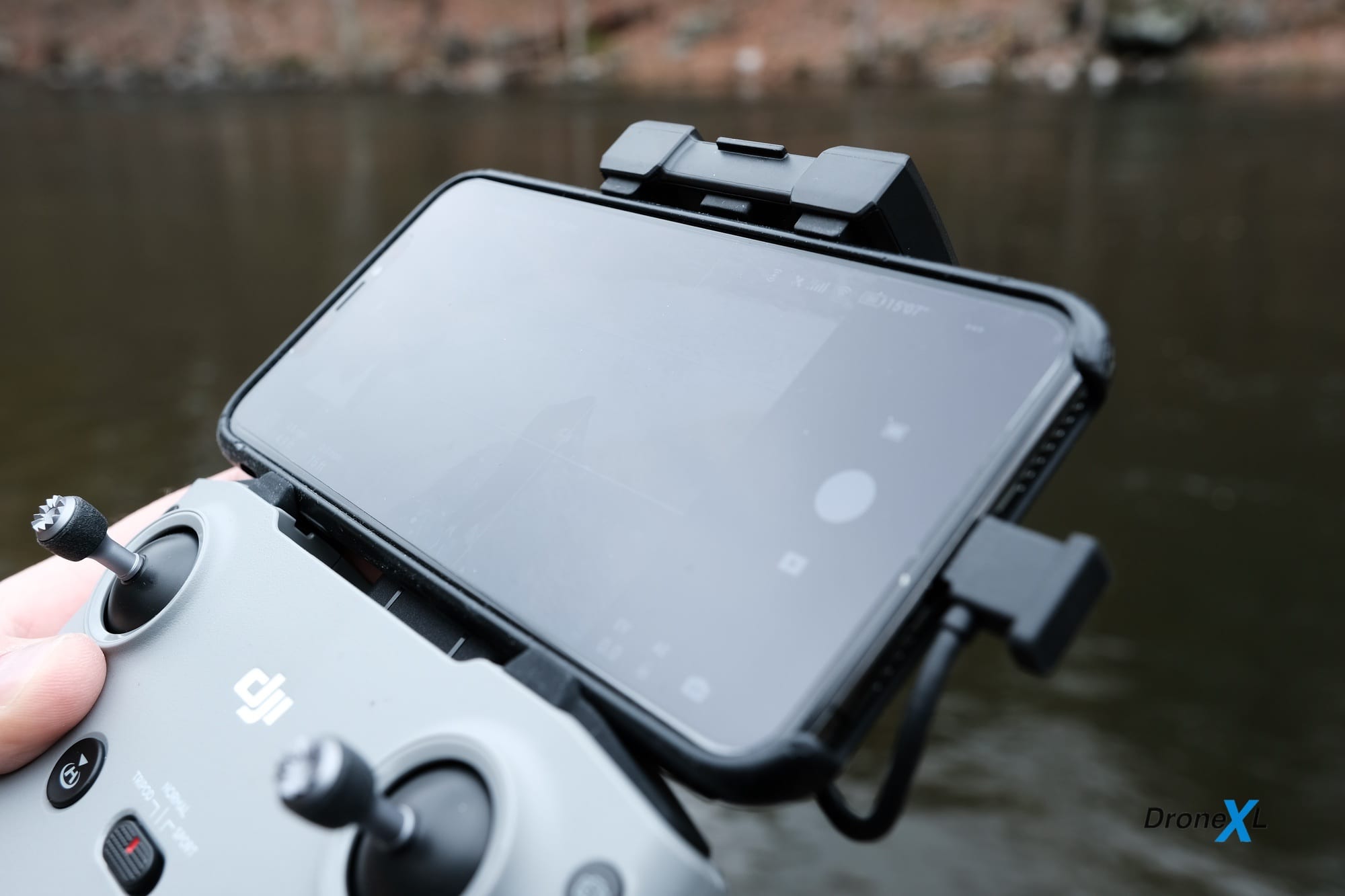 Hand holding a DJI Mavic Air 2 controller with a phone clamped above the sticks.