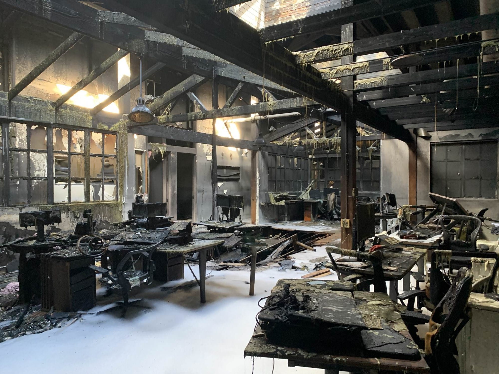 The gutted interior of the burned Airmap office with charred desks and fire foam underfoot.