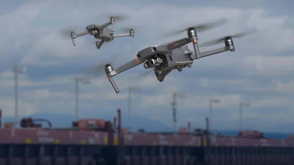Two DJI Mavic 2 Enterprise drones hovering above freight rail cars under cloudy skies.