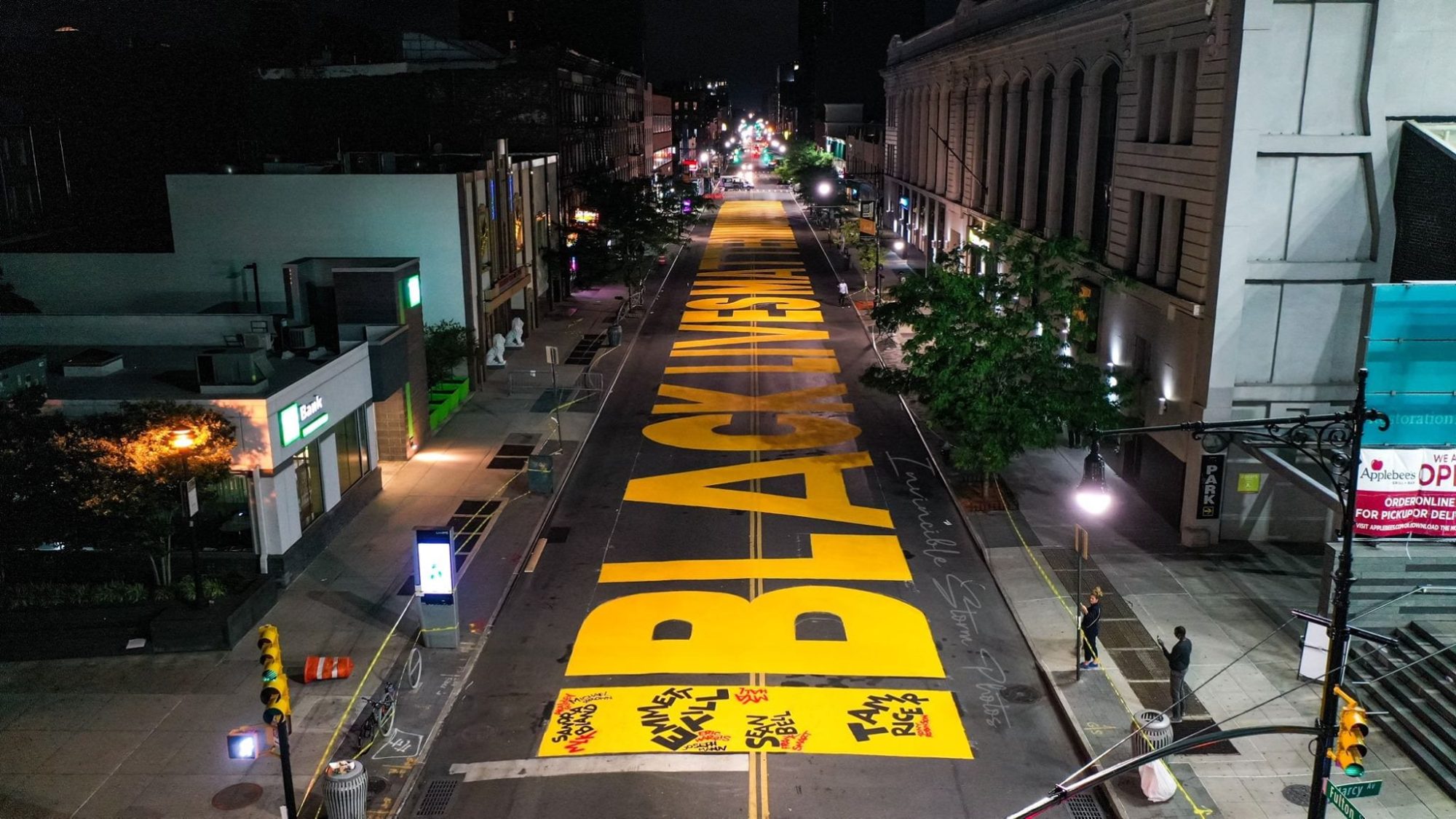 Aerial night view of BLACK LIVES MATTER painted in yellow down a city street.