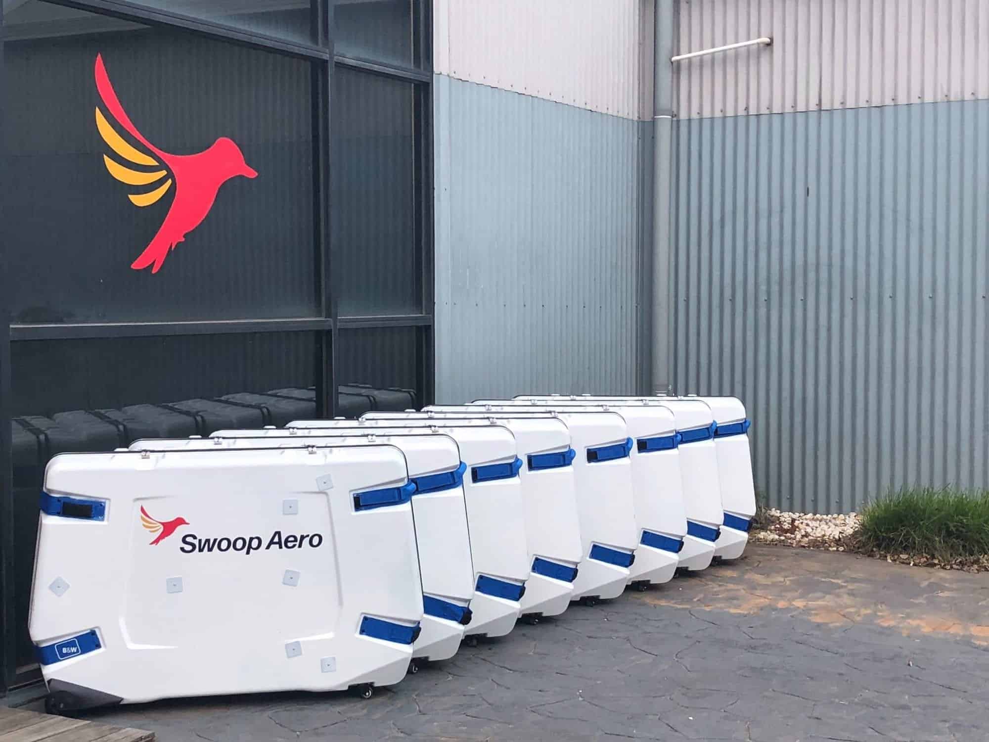 Row of white Swoop Aero transport cases outside a hangar bearing the bird logo.