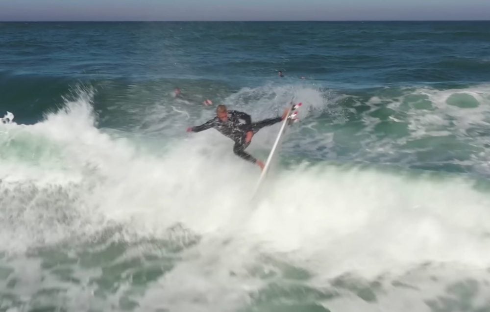 Surfer carving off the lip of a breaking wave, filmed from the air.