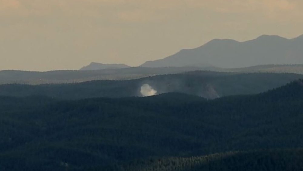 Smoke plume rising from forested ridges during a Colorado wildfire.