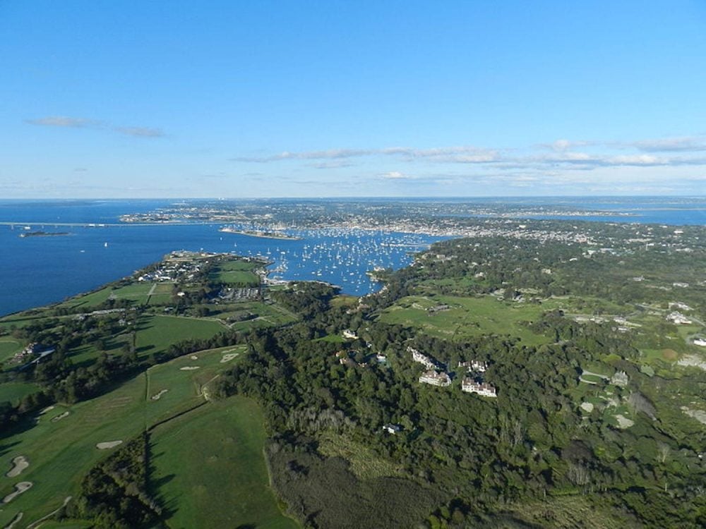 Aerial view of Newport, Rhode Island, with sailboats moored across the harbor and green coastal estates.