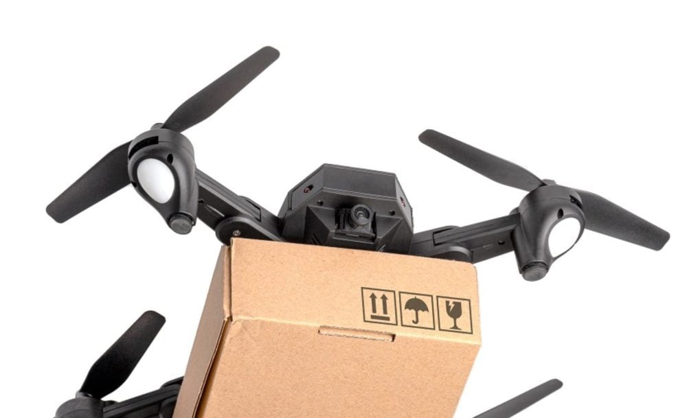 Folding quadcopter carrying a cardboard shipping box against a white background.