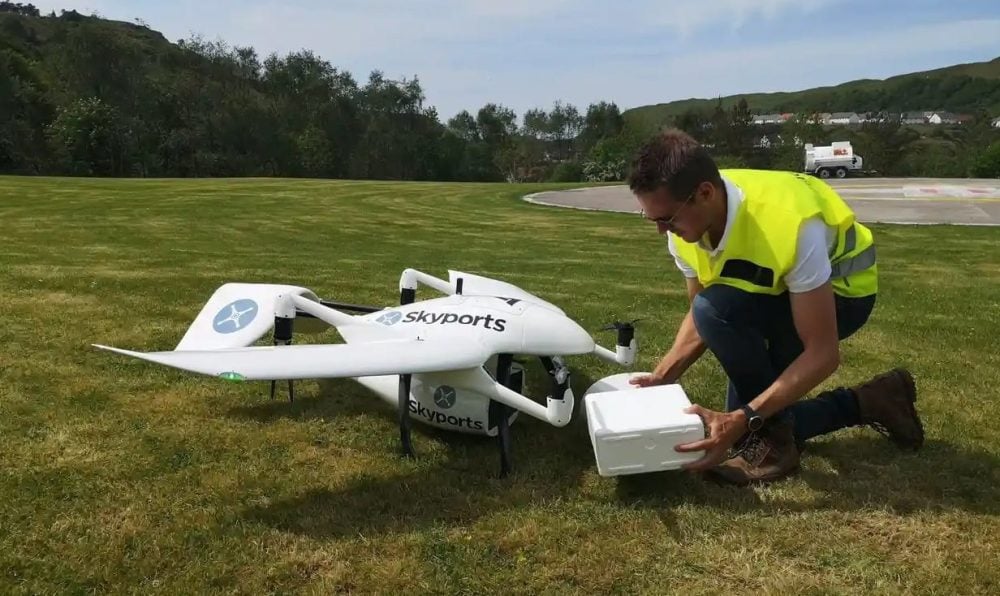 Worker in a hi-vis vest loads an insulated box into a Skyports delivery drone.