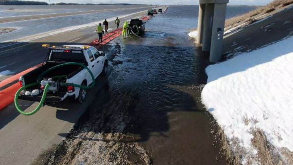 Aerial view of crews pumping floodwater across a snow-lined highway.