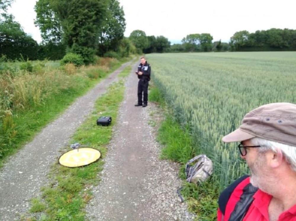 Search and rescue volunteer and a police officer beside a yellow landing pad on a farm track.
