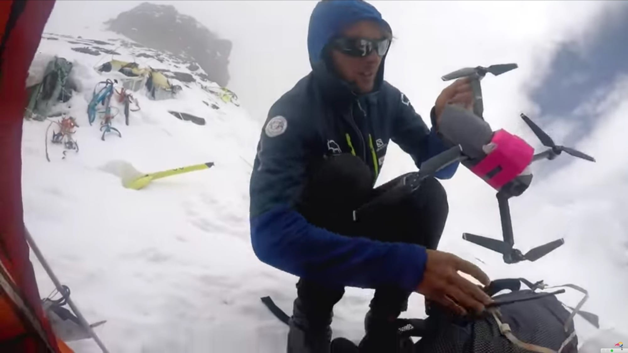 Climber on snow at altitude holding a Mavic drone carrying a pink payload package.