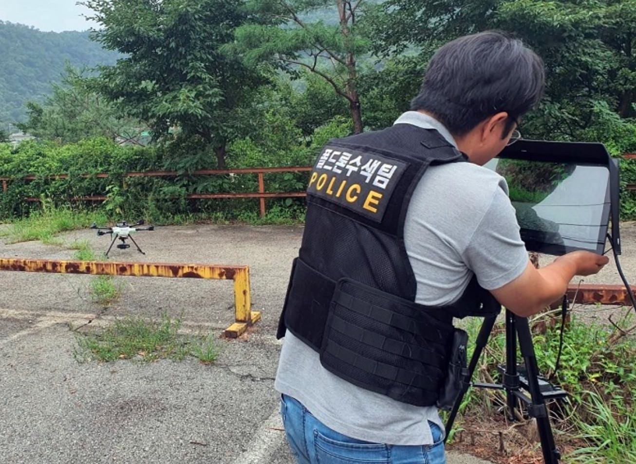 South Korean police drone operator monitoring a tablet beside a landed quadcopter.