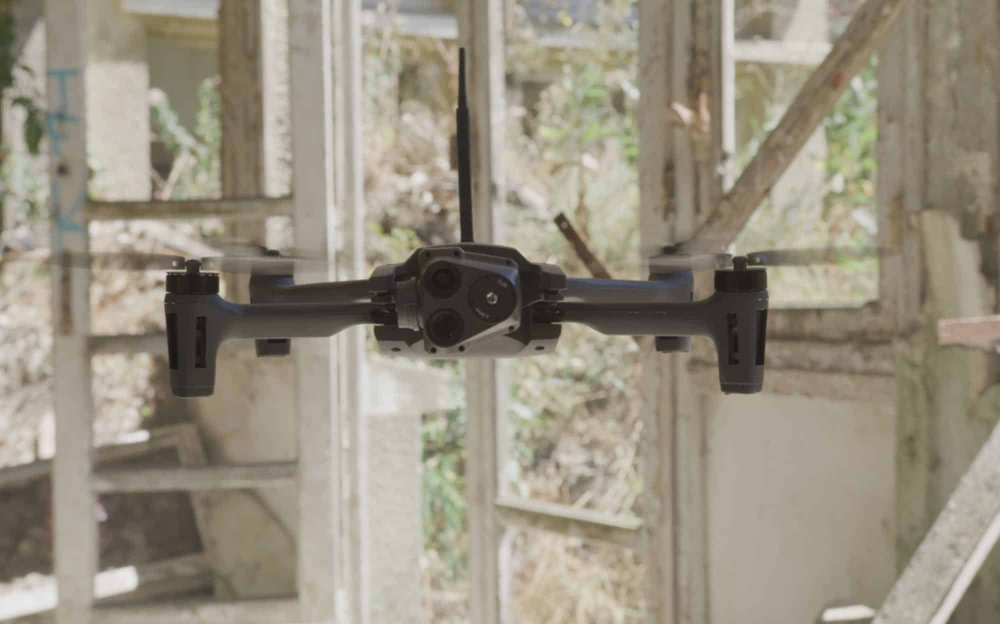 Skydio drone flying inside a derelict industrial building past a window frame.