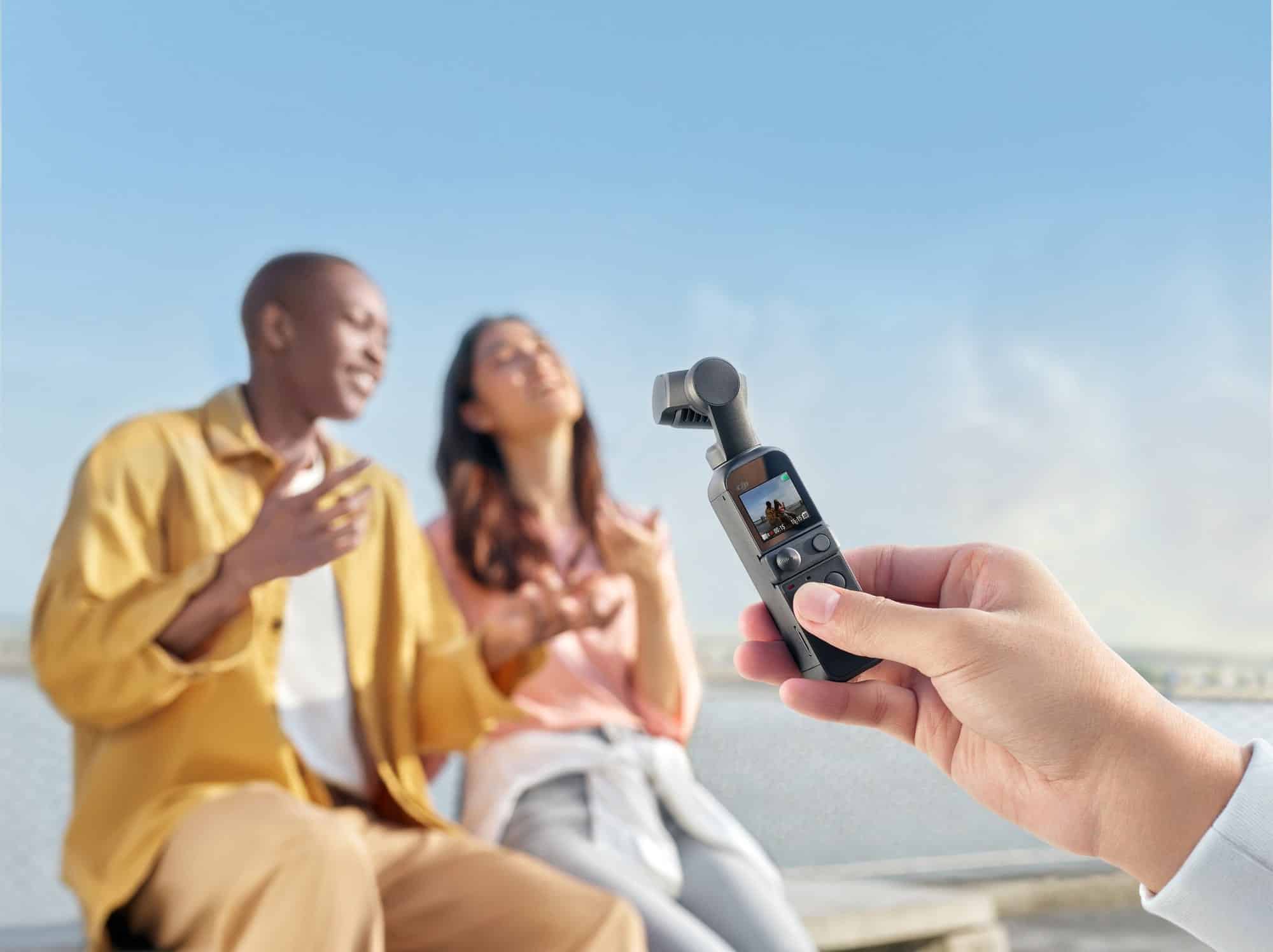 Person films a seated couple outdoors using a DJI Pocket 2 gimbal camera.