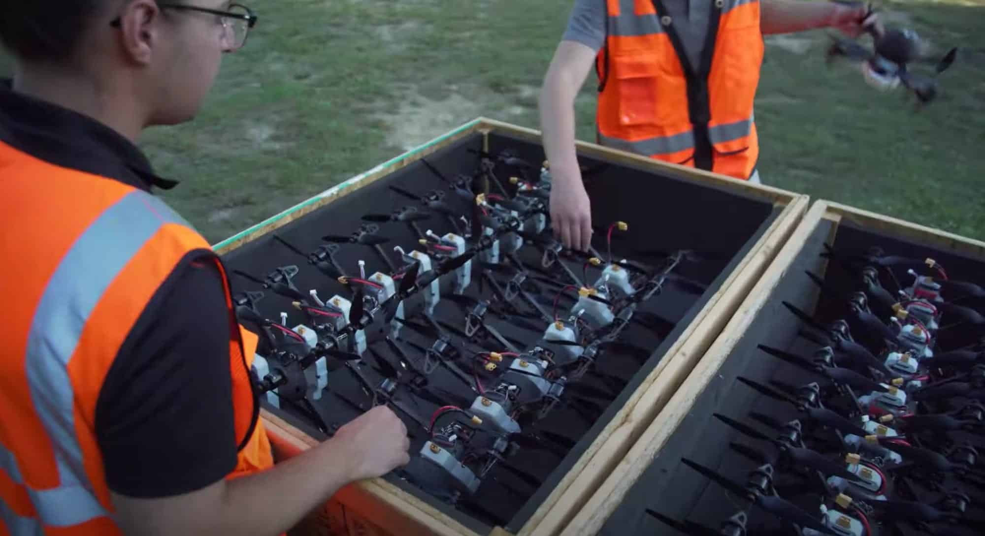 Crew in high-visibility vests unpacking rows of show drones from a wooden crate.