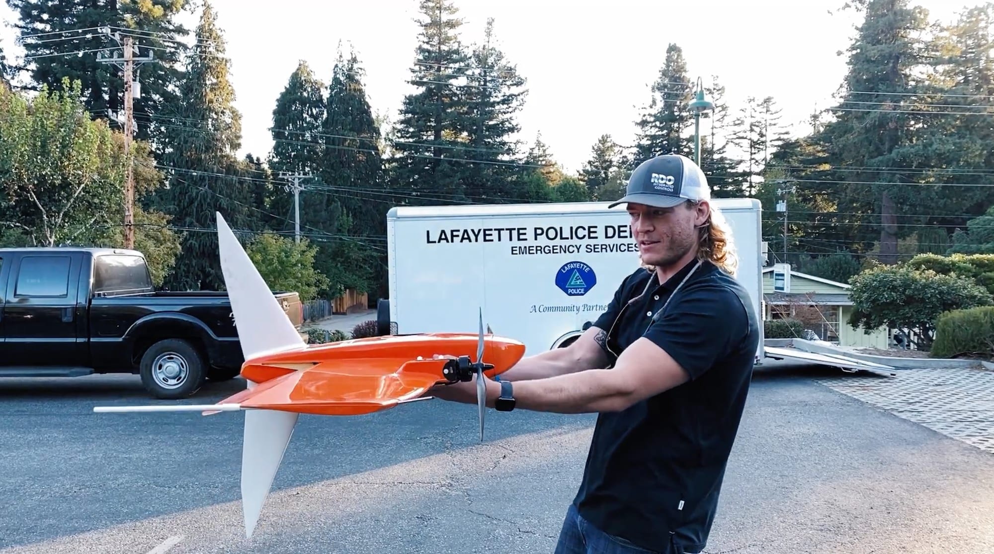 A drone operator holds an orange Wingtra VTOL aircraft outside a Lafayette Police trailer.