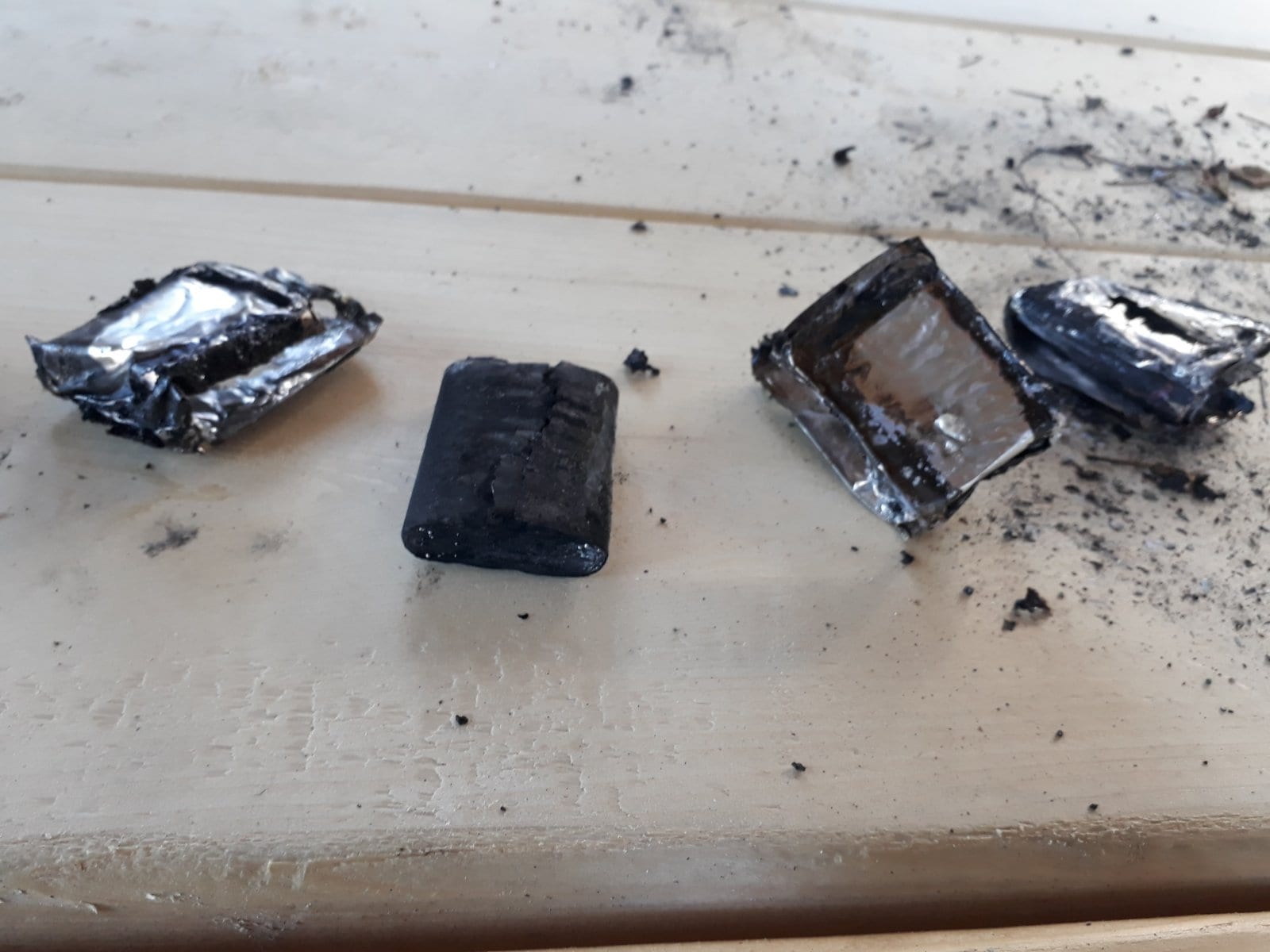 Charred battery cells and burnt debris from the drone spread across a wooden table.