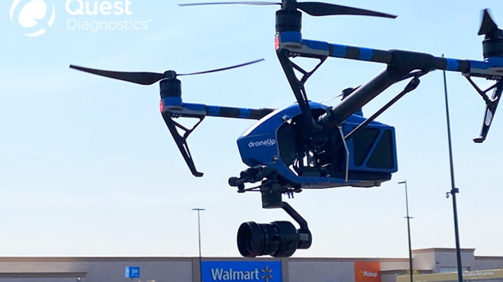 A blue DroneUp delivery drone flying in front of a Walmart store.