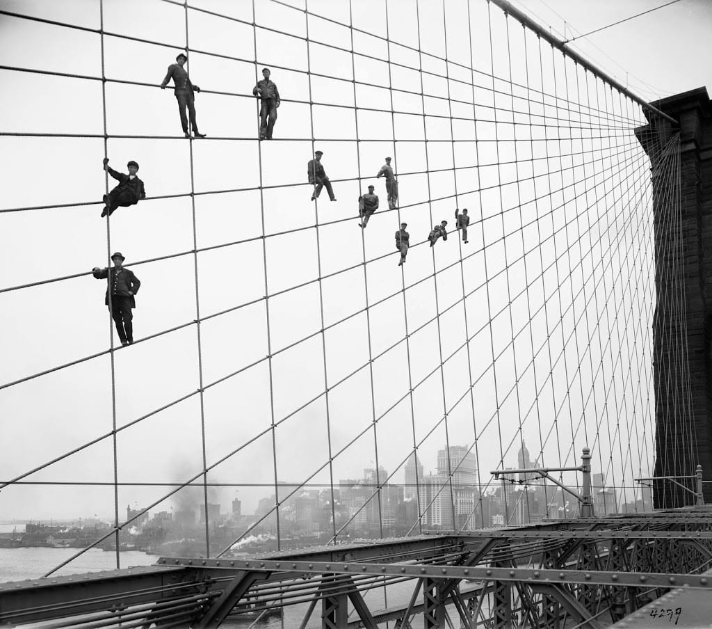 Historic photo of painters posing on the suspension cables of the Brooklyn Bridge.