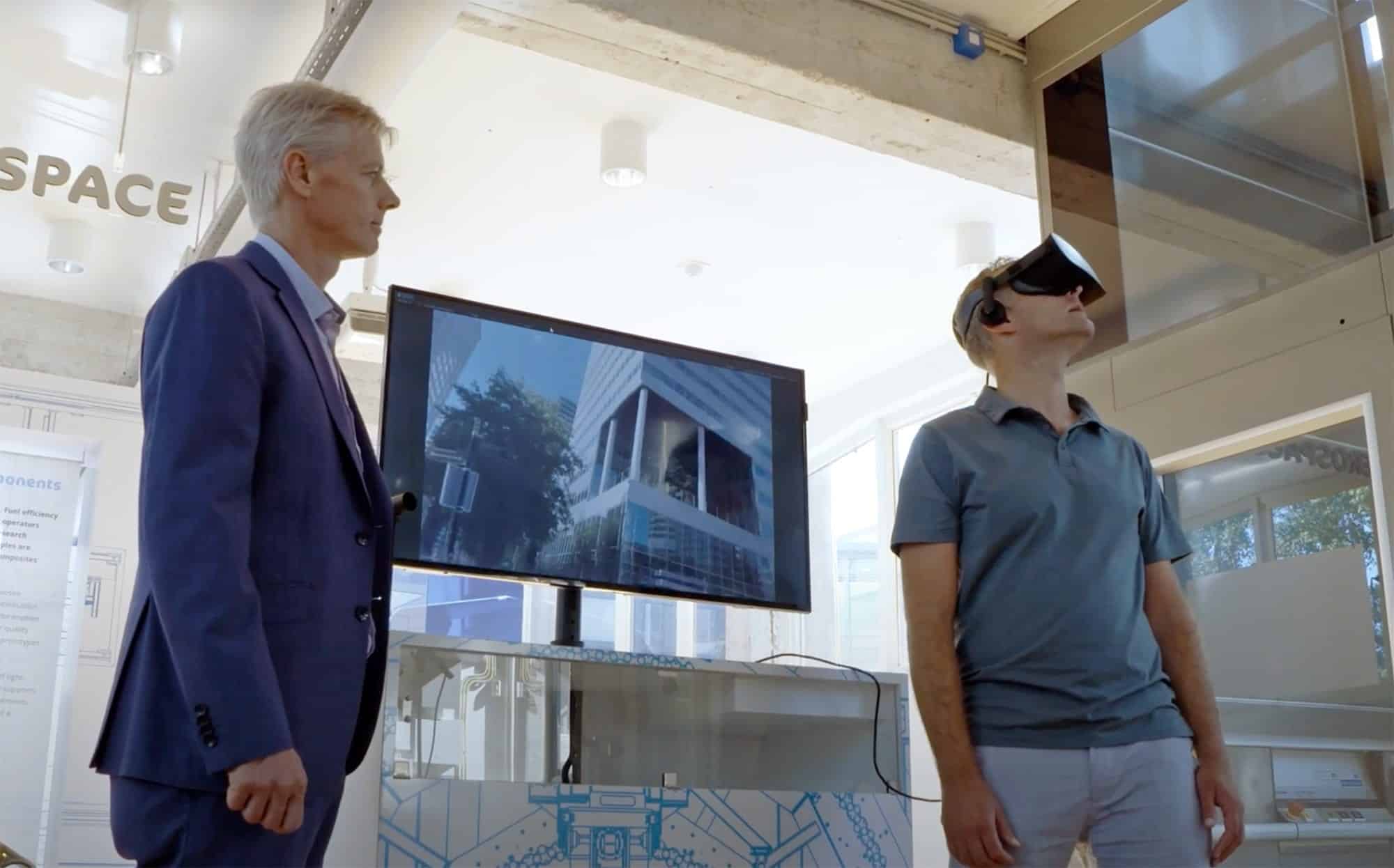 Researcher wearing a VR headset beside a screen in the noise simulator lab.