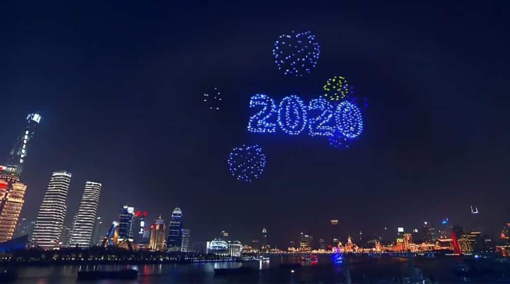 Drone swarm spelling 2020 in blue above a nighttime city skyline and waterfront.