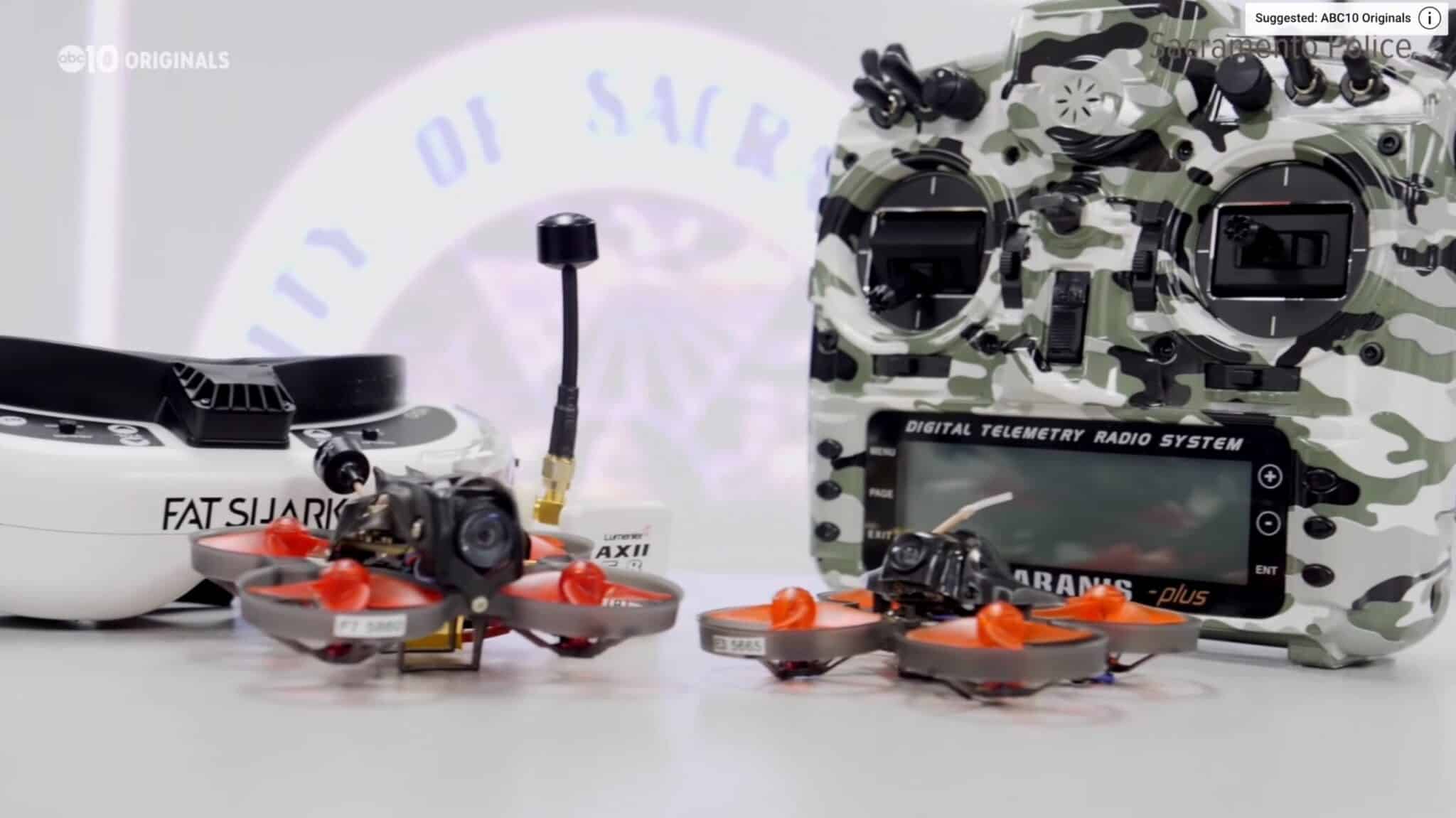 FPV goggles, camouflaged controllers, and two small cinewhoop quadcopters laid out on a table.