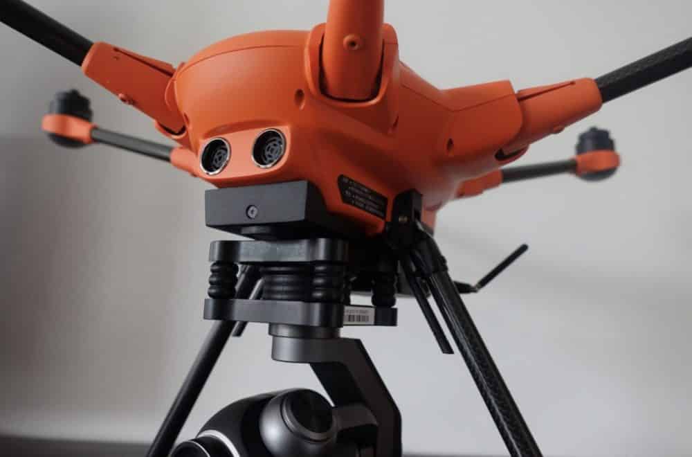 Close-up of an orange industrial quadcopter with a gimbal camera and folding carbon arms.