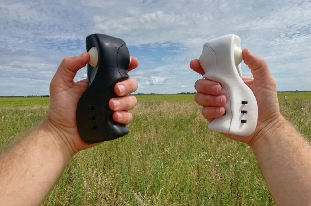 Two hands hold black and white one-handed drone controllers above a grass field.