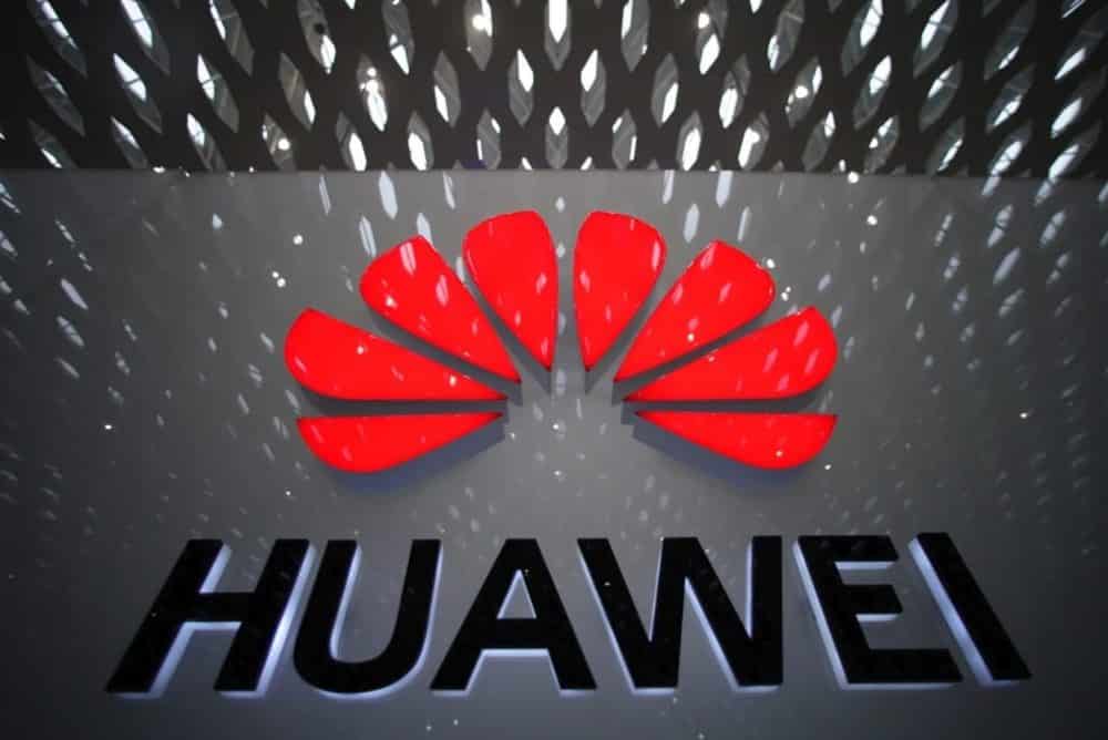 Illuminated red Huawei logo and wordmark mounted on a dark textured wall.