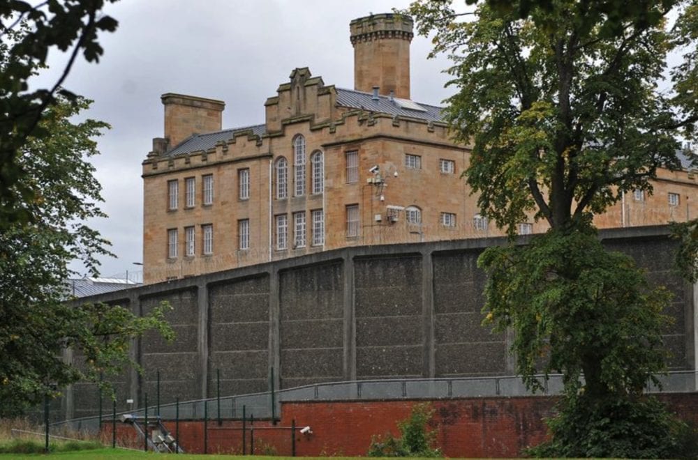 A stone Victorian prison building rising behind its high perimeter wall.