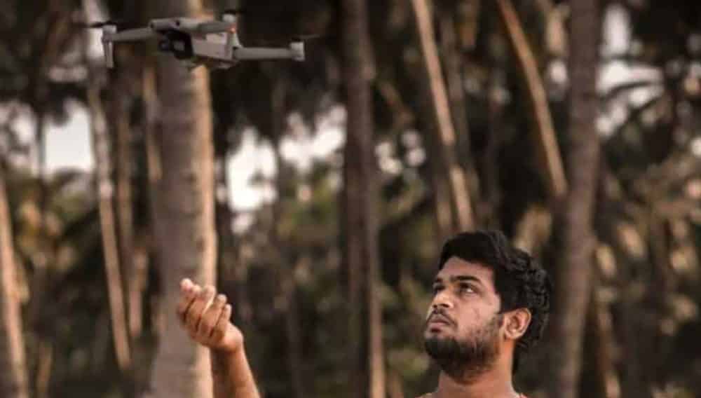 A young man hand-launches a DJI Mavic drone among coconut palms in Kerala, India.