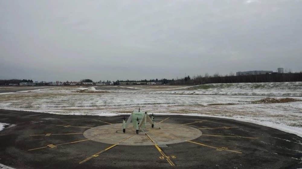 A pale tail-sitting cargo drone waits on a helipad in a snow-dusted field.