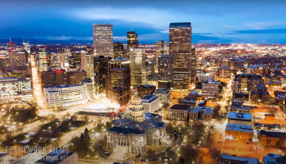 Aerial dusk view of a downtown skyline with a lit capitol dome below.