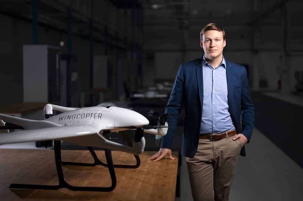 Wingcopter co-founder Tom Plümmer stands beside a Wingcopter fixed-wing delivery drone.