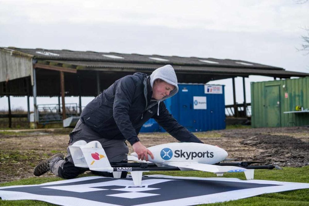 An operator prepares a Skyports fixed-wing delivery drone on a landing pad at a farm.