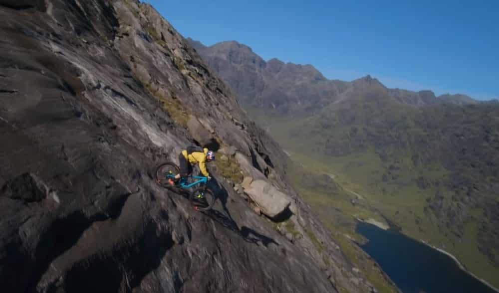 Mountain biker Danny MacAskill riding across a near-vertical rock slab above a Highland loch.