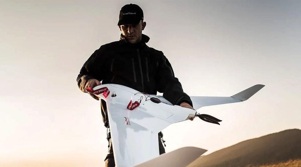 An operator holding a white C-Astral fixed-wing drone ready to launch at dusk.