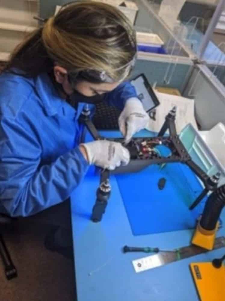 Technician in a blue coat assembles a drone airframe at a workbench.