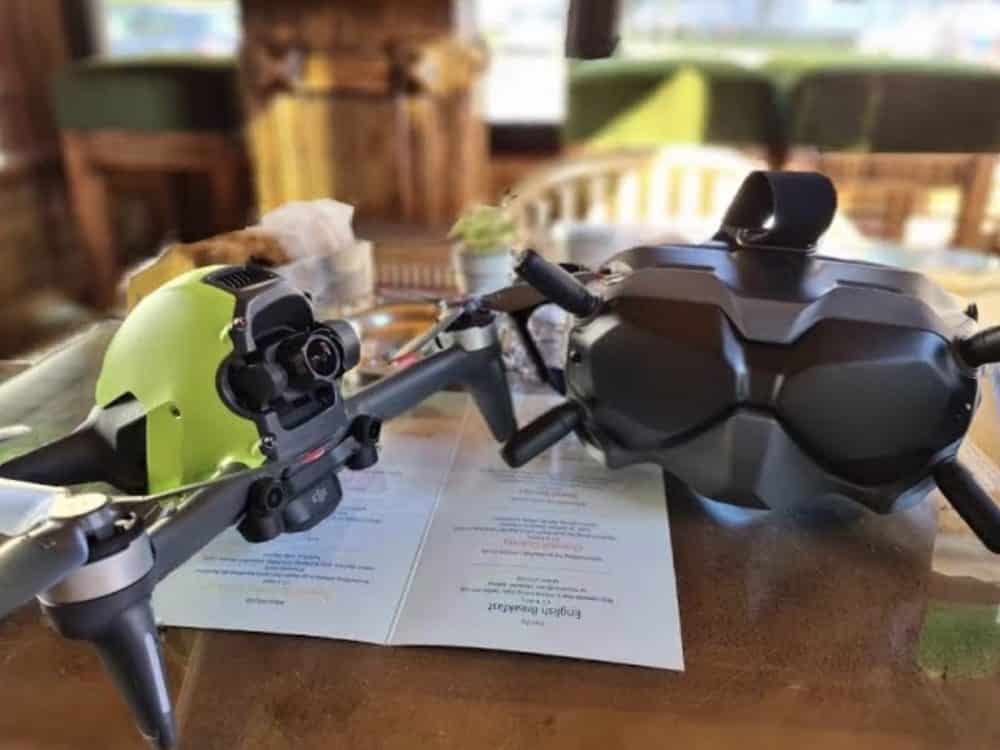 Lime green DJI FPV drone and its goggles resting on a wooden restaurant table.