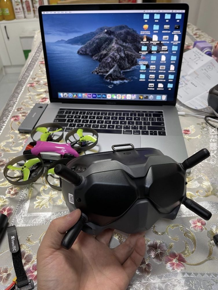 DJI FPV goggles held in front of a laptop with a small tinywhoop drone alongside.