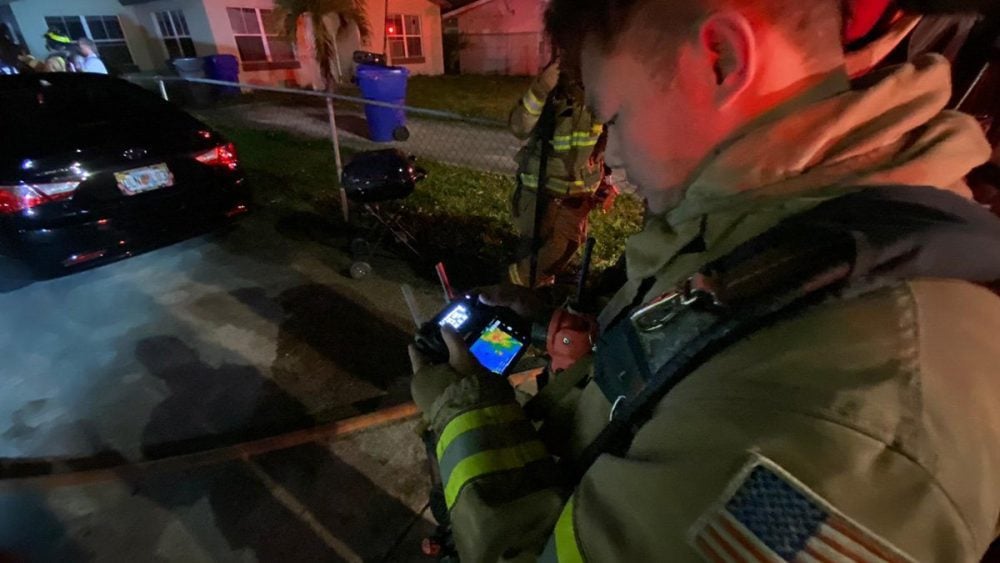 Firefighter checks a thermal drone feed on a controller screen at a night callout.