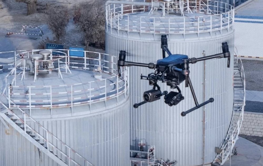 DJI Matrice enterprise drone hovers above cylindrical industrial storage tanks.