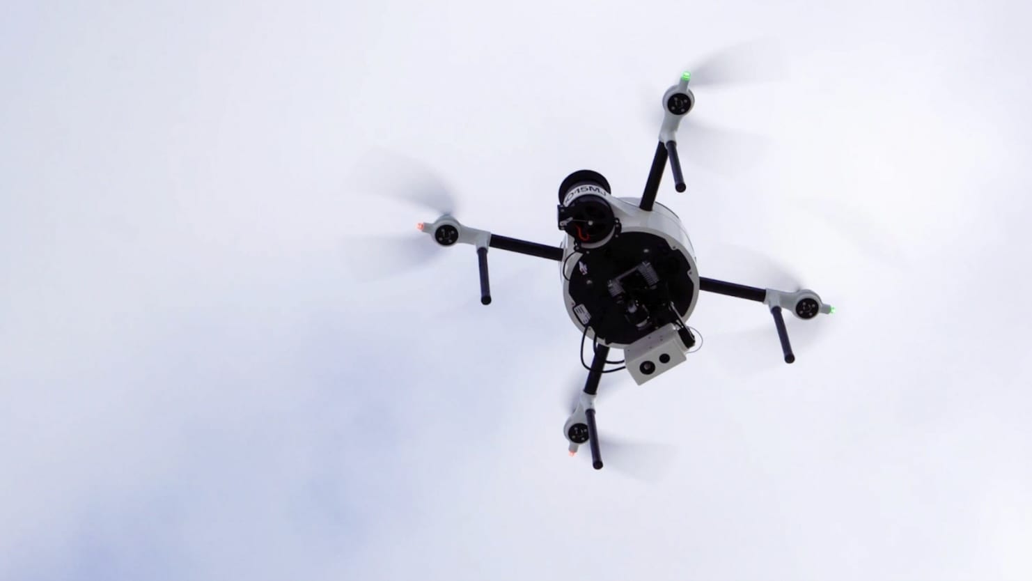 Small camera quadcopter climbing against a flat white overcast sky.