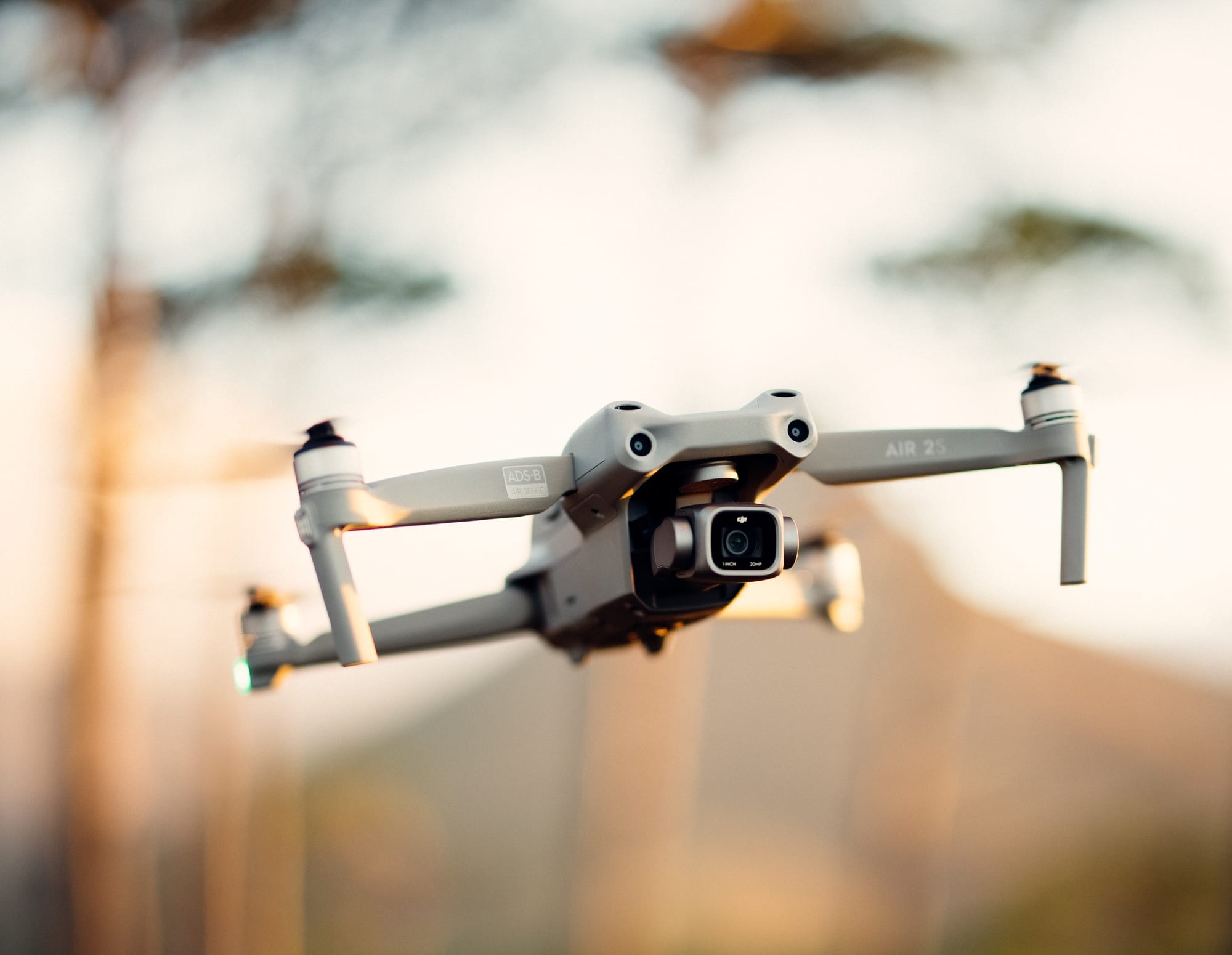 The DJI Air 2S hovers at golden hour with its gimbal camera forward.