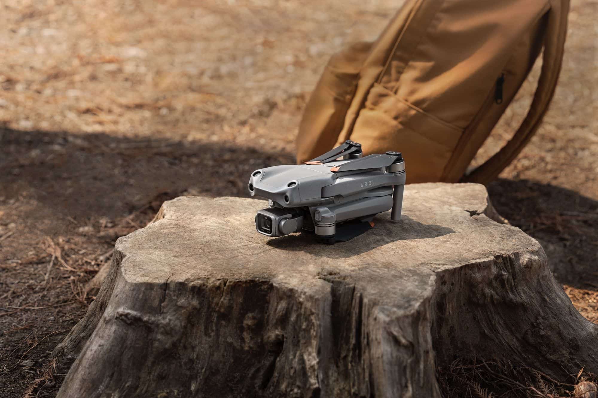 A folded DJI Air 2S rests on a tree stump beside a tan backpack.