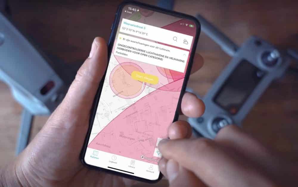Hand holding a phone showing a red restricted airspace zone beside a drone controller.