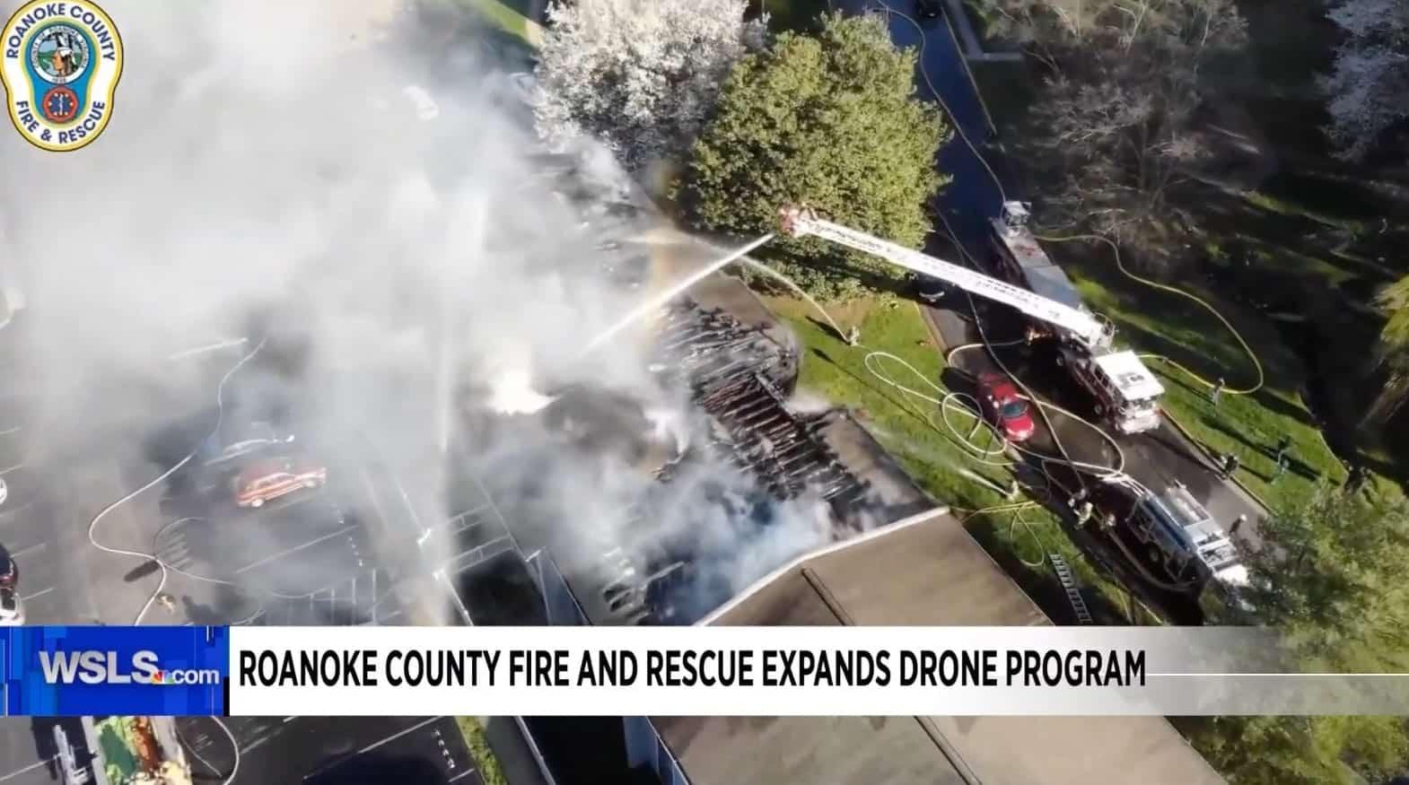 Aerial news frame of crews spraying water on a smoking fire scene.